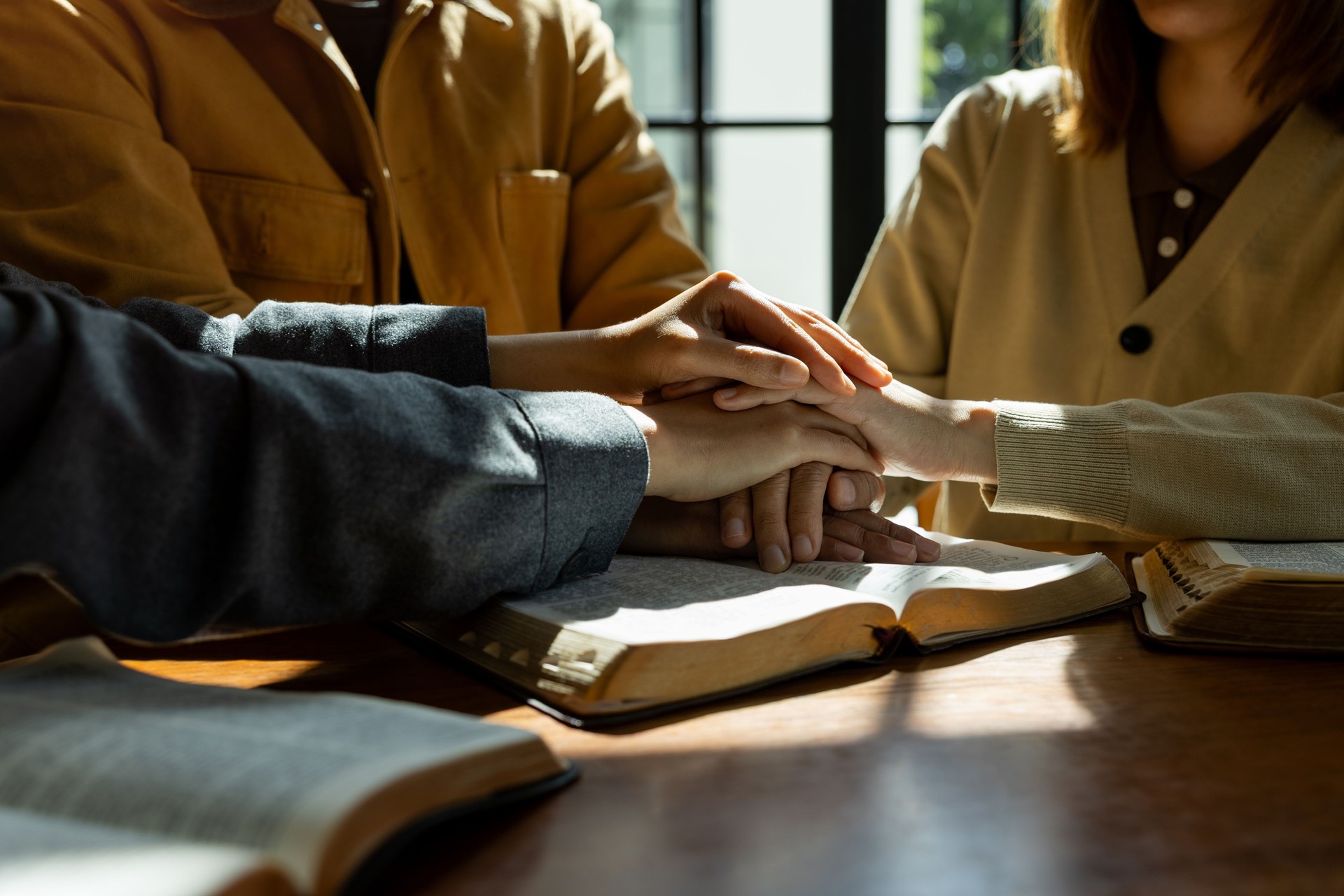 Christian group of people holding hands praying together over holy bible.