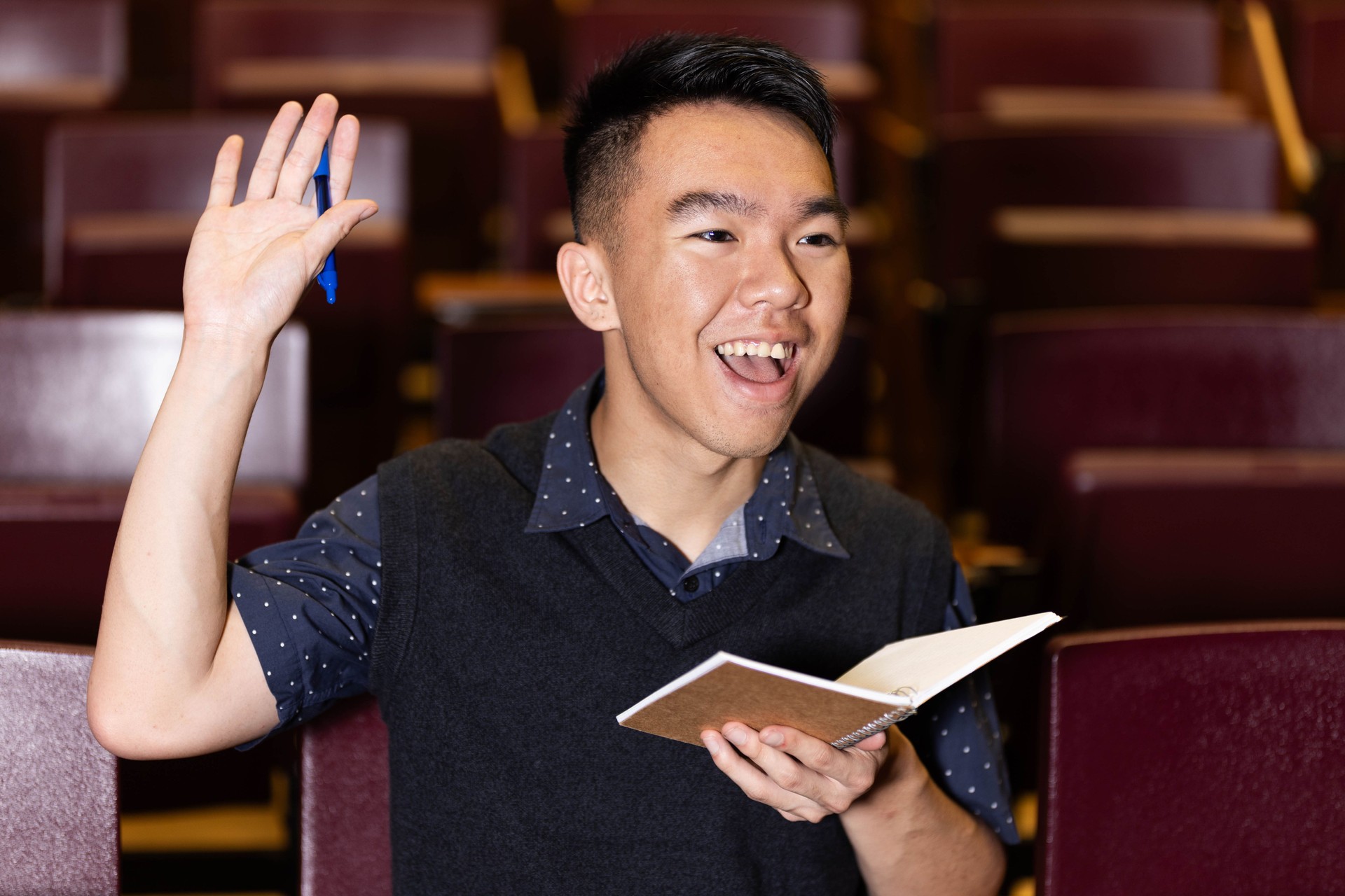 A college student holds a notebook and raises hand in the lecture hall