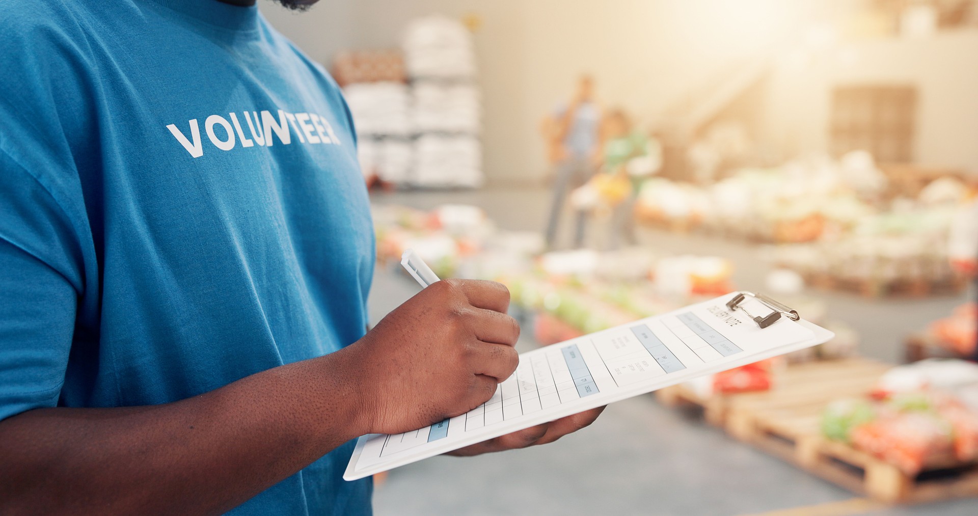 Clipboard, pen and hands of volunteer writing for charity, non profit or donation stock list in community center. Inspection, notes and male NGO worker with inventory for food drive with information.